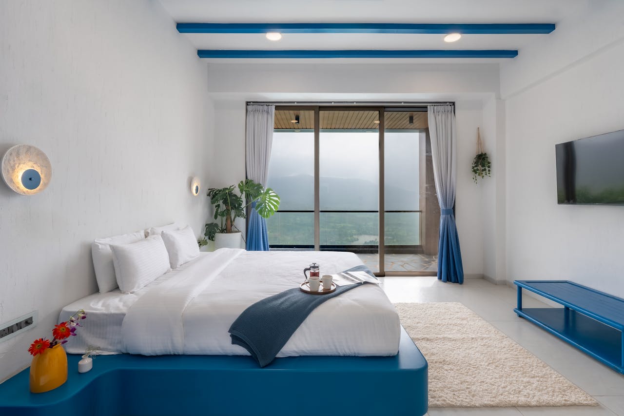 Bright white minimalist bedroom featuring large windows with a mountain view and cozy decor.